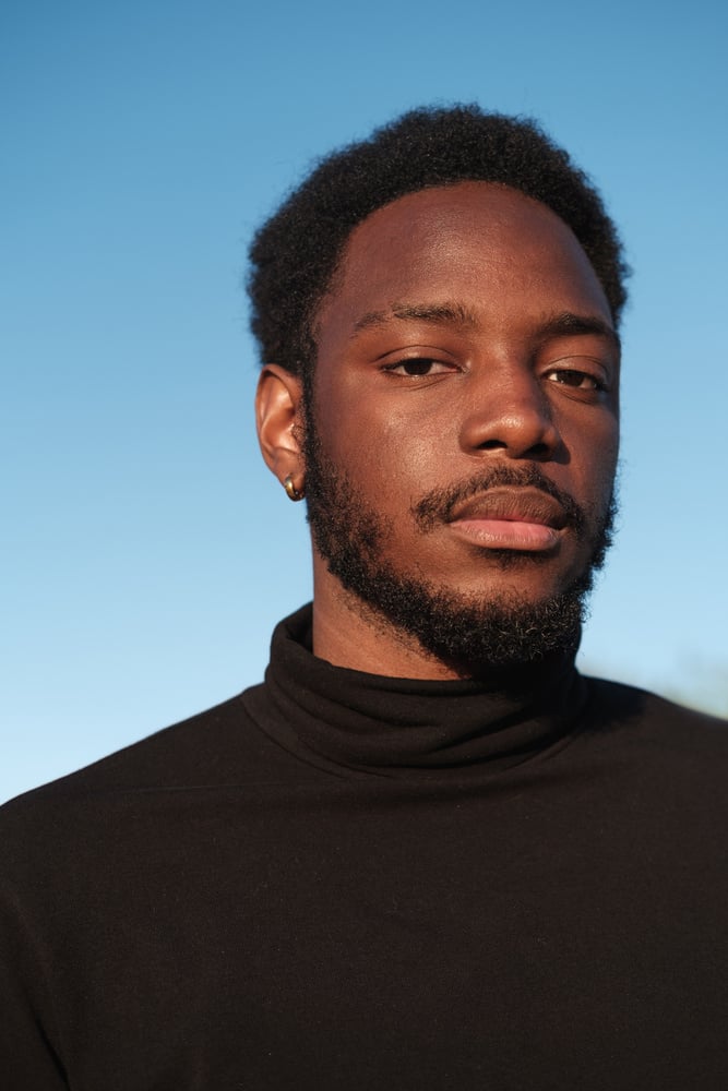 a person in a black turtleneck shirt against a blue sky.